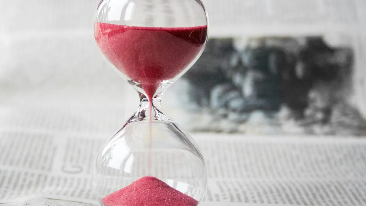 Close-up of a transparent hourglass with pink sand flowing, placed on a newspaper background.